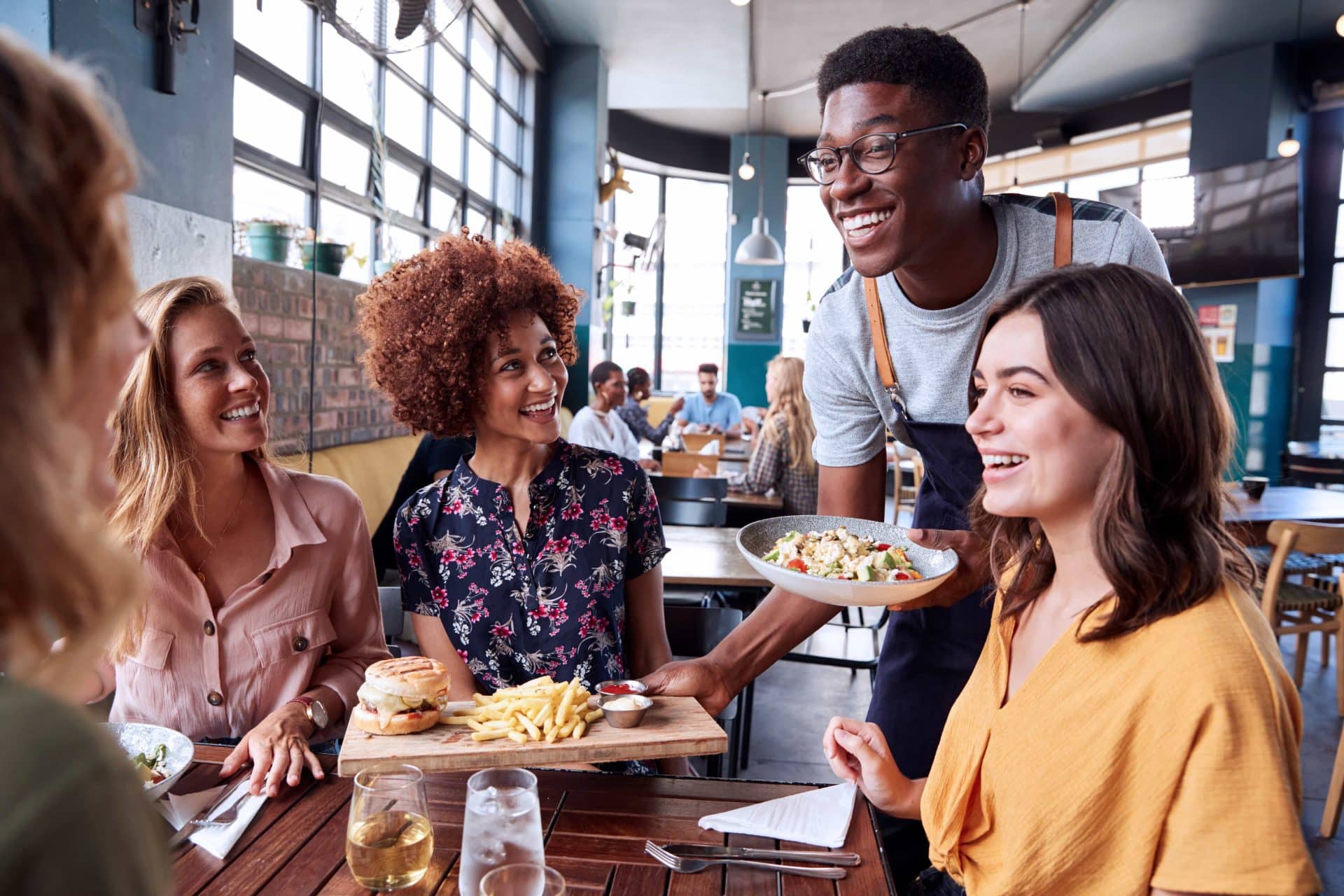 young waiter bringing food to a table of professional women gathered for lunch