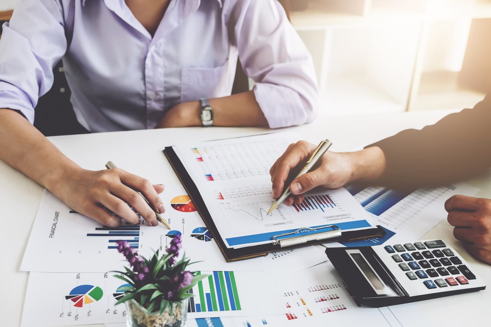 two financial managers reviewing portfolio information on a clipboard within a scattered arrangement of various reports